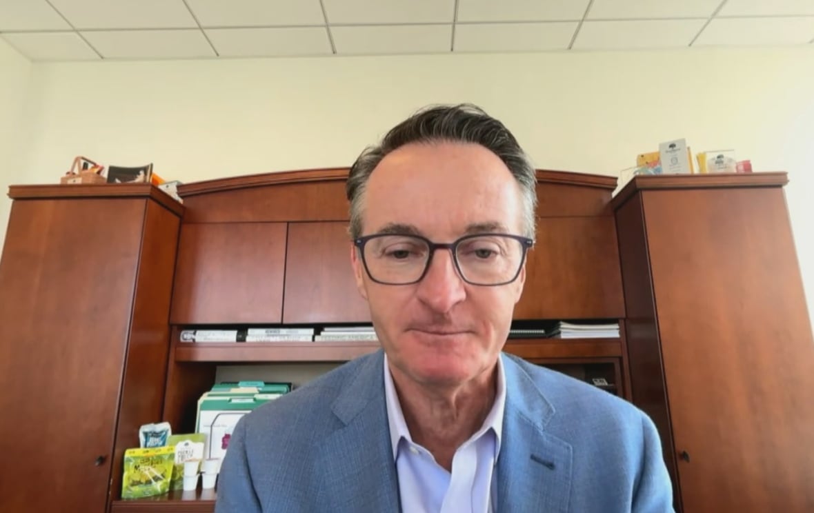 A man with vessels and a suit jacket is in front of a desk.
