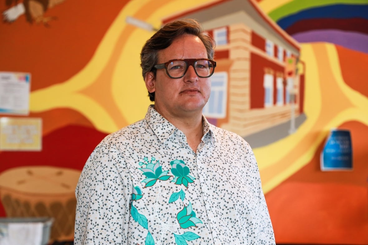 A man with glasses looks at the camera.