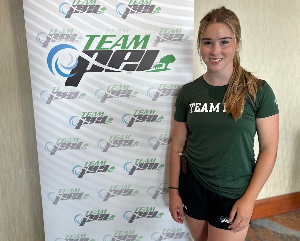 A teenaged girl in a green and white T-shirt and shorts stands in front of a poster that says Team P.E.I. 