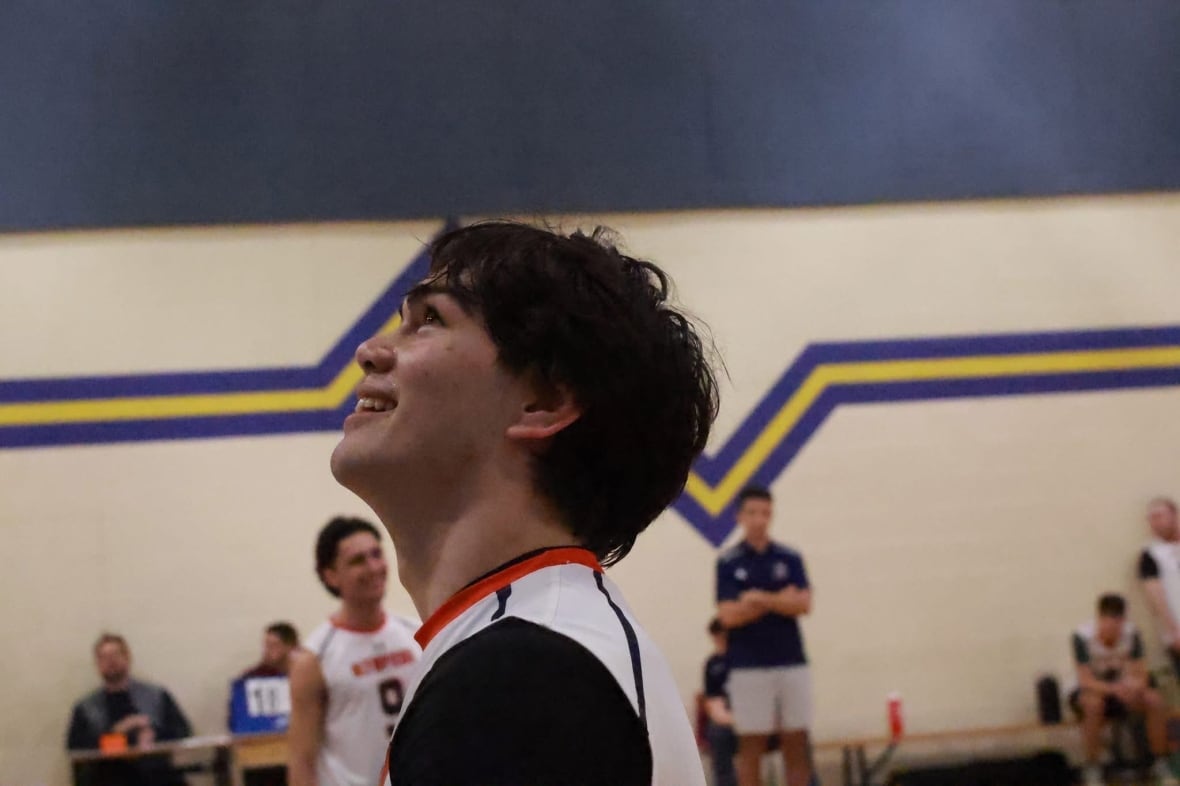 A young man stands on a volleyball court.