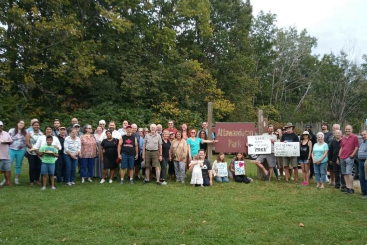 A bunch of people stand beside a park sign.