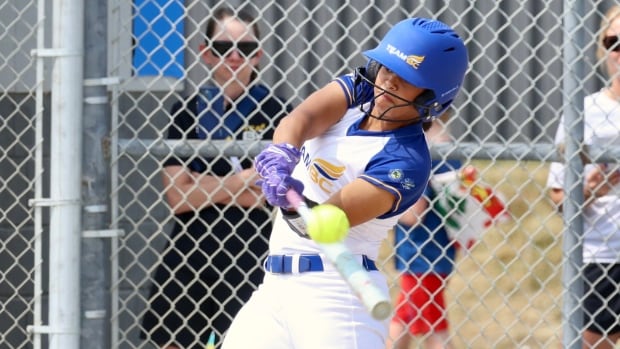 A women's softball player is shown swinging a bat and making contact with a softball.