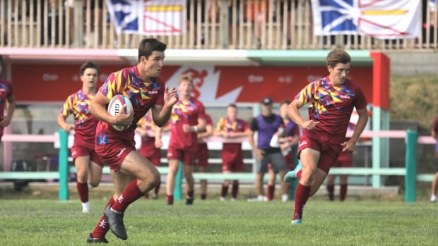 A player charging forward with the ball, with Newfoundland and Labrador flags visible in the background.