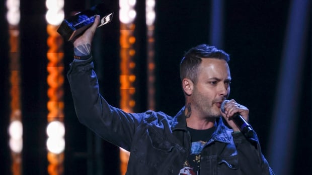 A man speaks into a microphone while holding up a trophy.