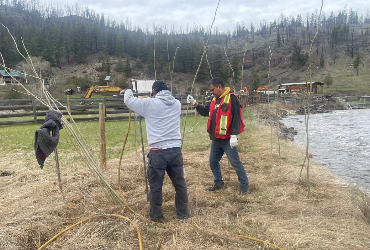 Two men sticking a pipe into the ground near a river