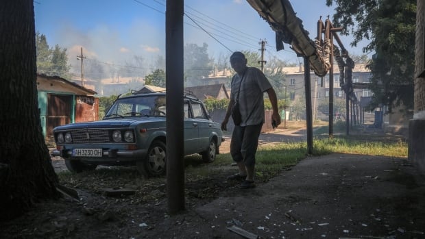 A man walks on the street after an apartment building was hit by a drone strike. To his right is a blue car.
