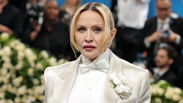 An older blonde haired woman is shown in closeup wearing a white outfit.