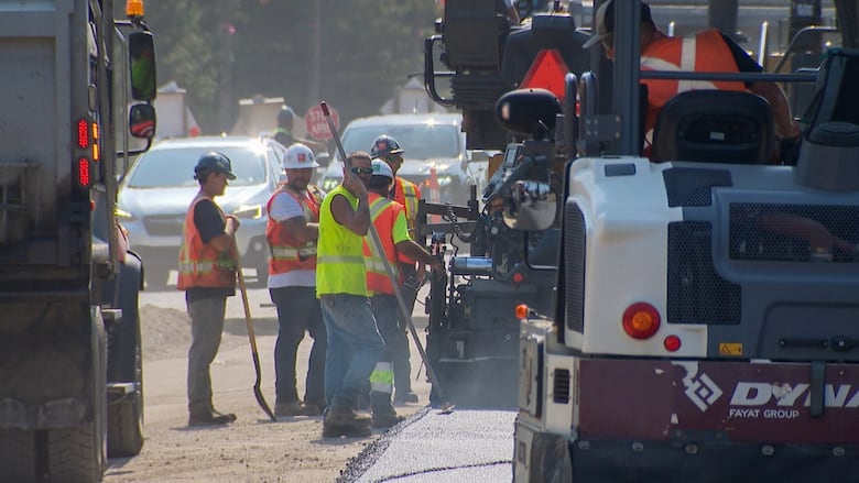 Road construction workers laying new asphalt on a sunny day.