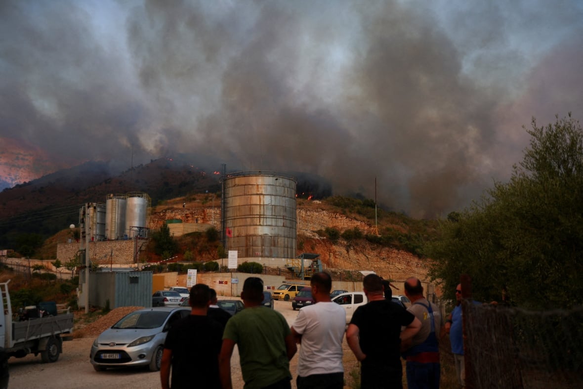 People watch smoke rising from a fire near town buildings.
