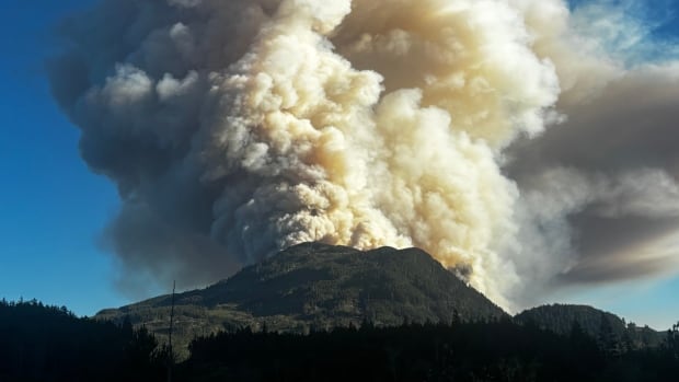 Smoke billows into a blue sky behind a mountain peak.