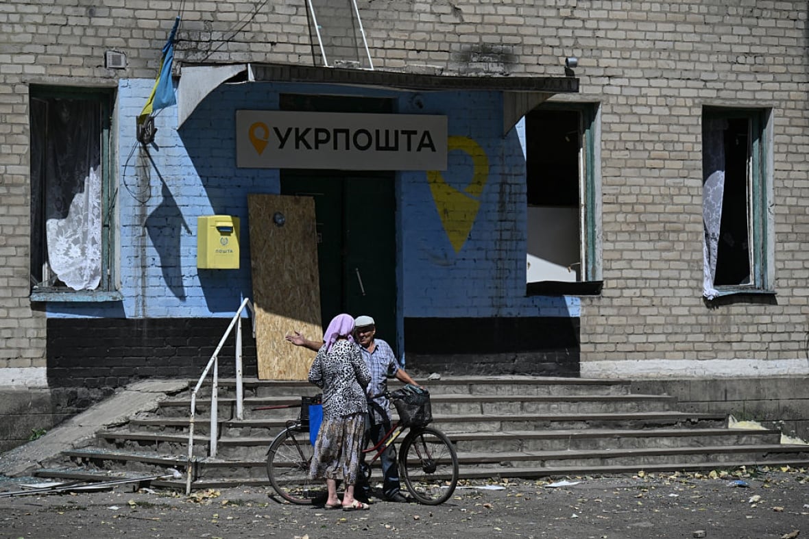 Two people are talking to each other, in front of a damaged post office in Biluski, Ukraine.