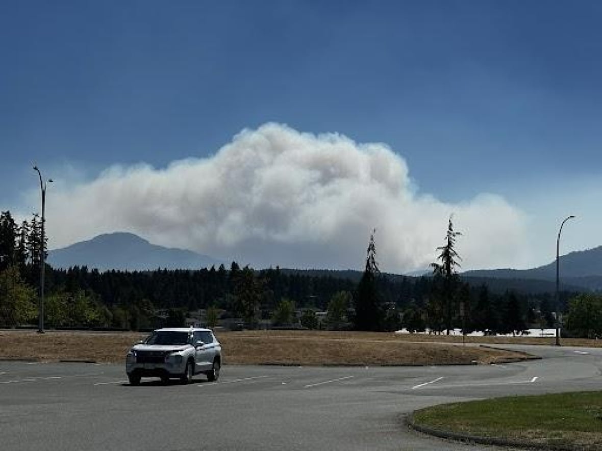 Smoke arises from hills above a parking lot with a lone car there.