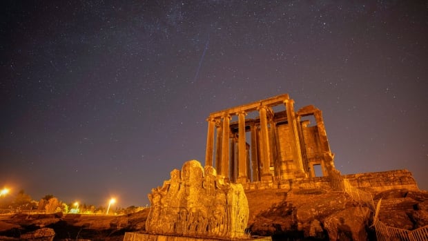 Meteors streak across the night sky, with a temple in the foreground.