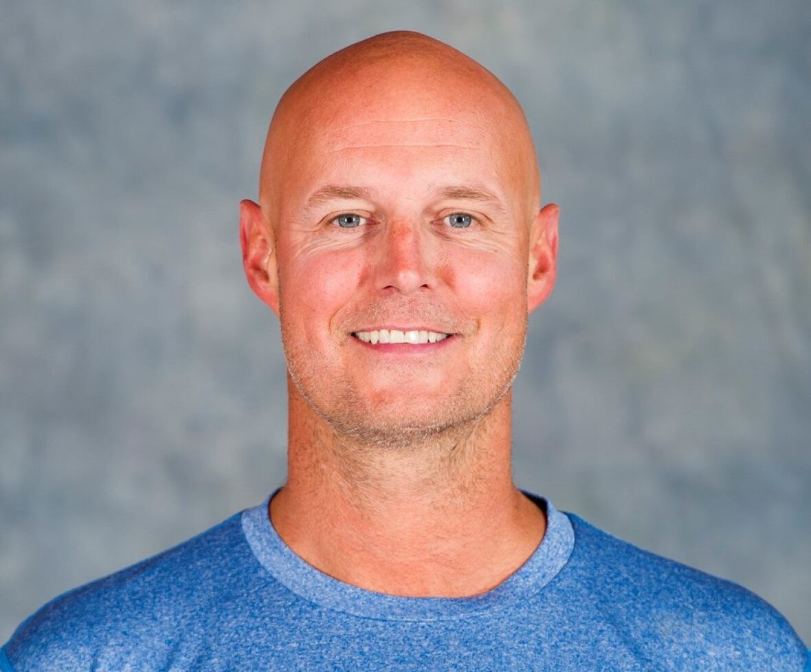 A man in his 40s with a shaved head smiles at the camera while wearing a blue t-shirt