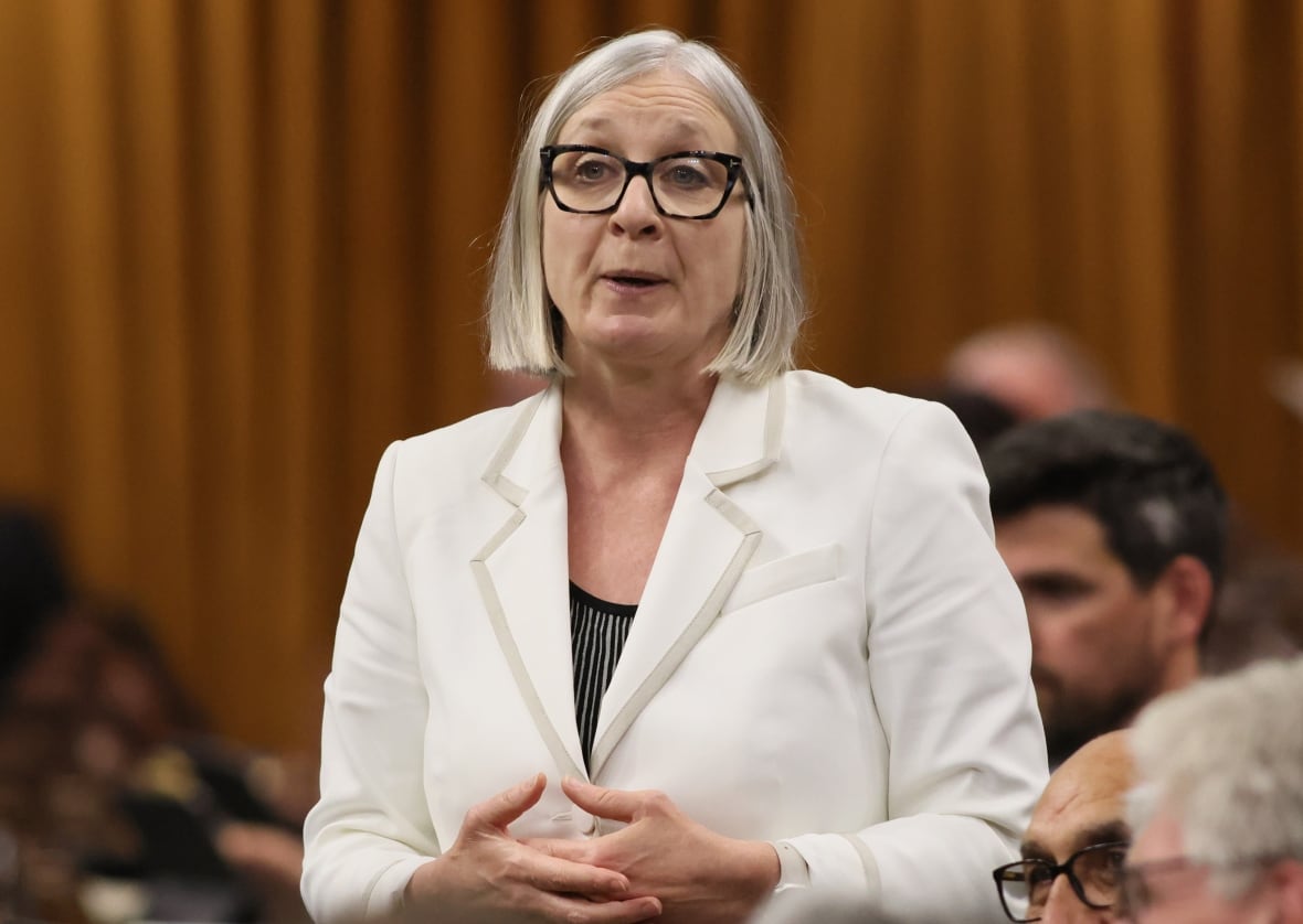 A woman in a white blazer stands and speaks in the House of Commons.