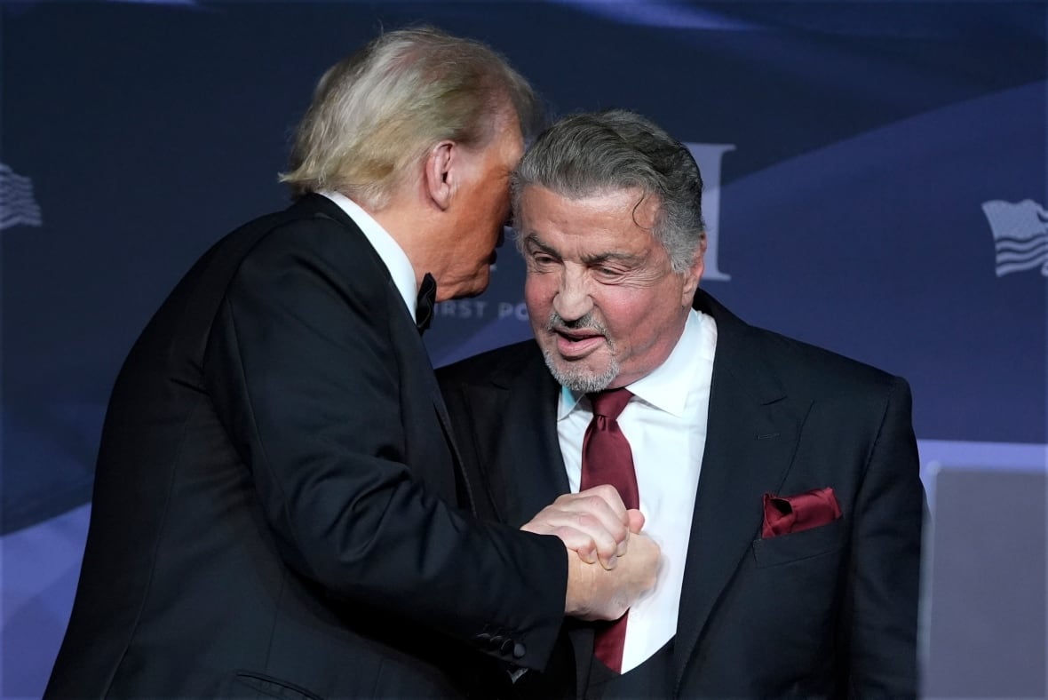 Zwei Männer in Anzügen fassen sich auf der Bühne an den Händen und umarmen sich.