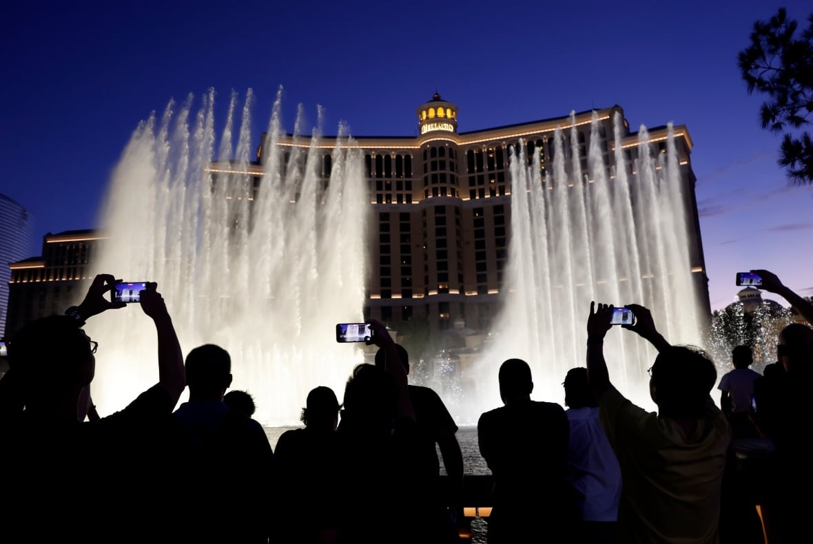Visitors in a silhouette watch and take portable shots in fountains from Bellagio Water, at night.