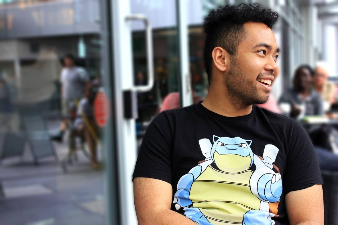 Un uomo sorridente che guarda di lato e indossa una maglietta dei Pokémon.