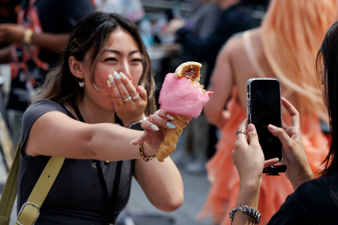 Cupping her mouth, a woman holds up a butter tart cotton candy while another person takes her photo with a cellphone at a fair.