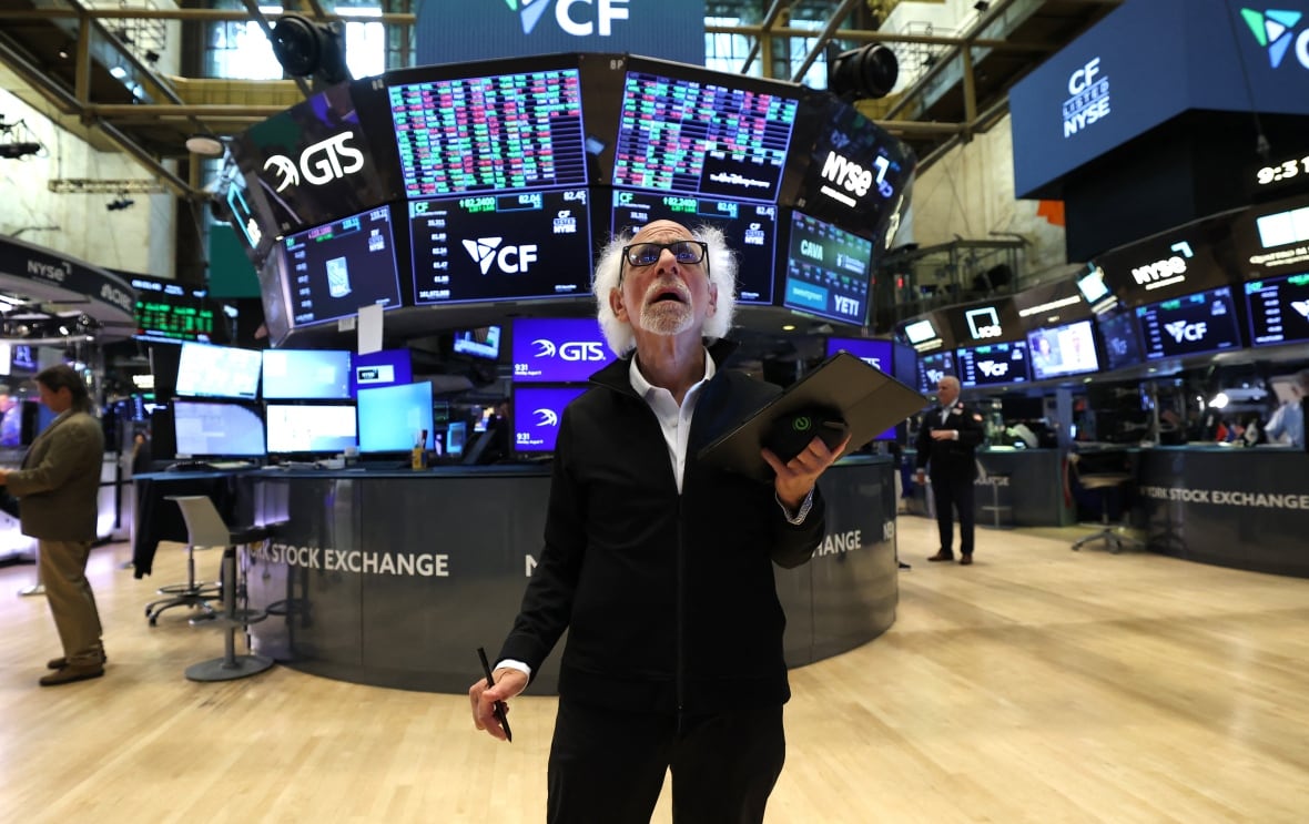 A person looking up stands on the floor of a stock exchange.