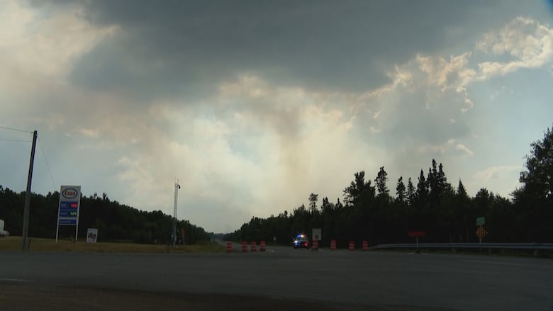 An intersection, blocked by pylons and a police car, with plumes of smoke overhead
