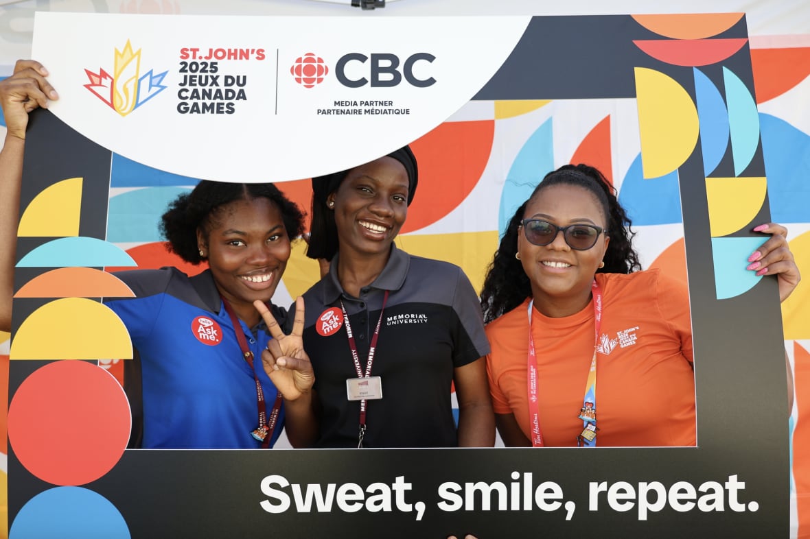 Three women holding up a large CBC and 2025 Canada Games photo frame in the CBC Pop-Up Photo Studio. One women in the middle is holding up two fingers as a peace sign.