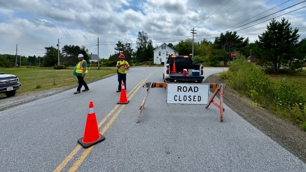 A rural road with two men in caution vests and a sign that says road closed.