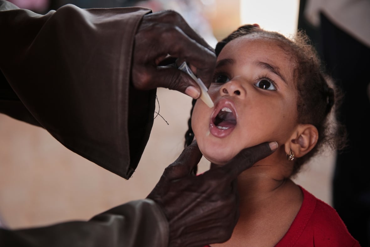 Adian adults adhere to a small girl and press a small package of medicine in her open mouth. 