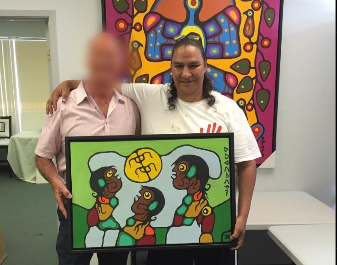Two men, one of whos face is blurred, stand arm in arm holding a painting. His name appeared on many certificates of authenticity linked to forgeries. In this picture from 2016, he poses with the buyer of a forgery entitled 'Brothers on Green'.
