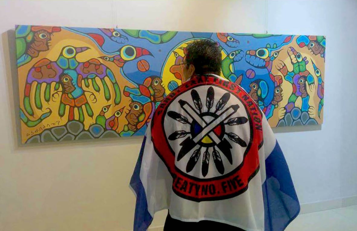 A man wearing a flag over his shoulders stands in front of a painting