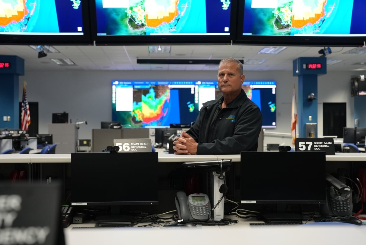 A man sitting in an office surrounded by television.