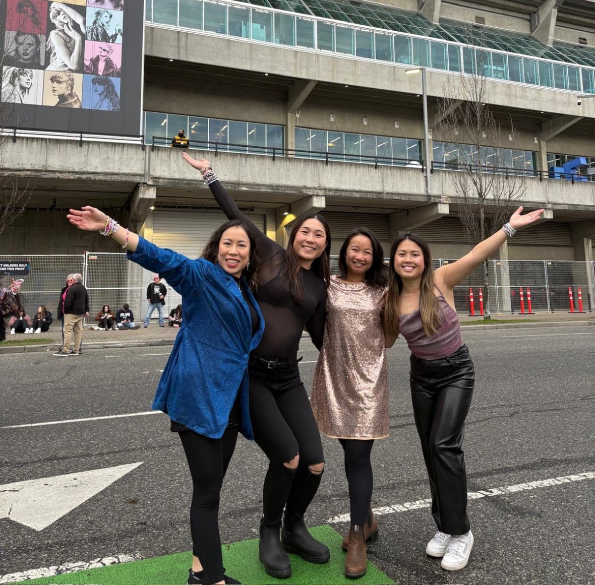 A group of four women smile in front of BC Place that's decorated in Eras Tour decorations. 