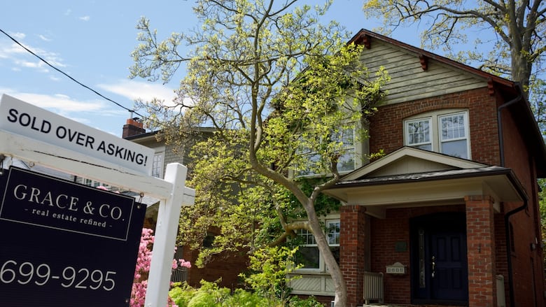 A real estate sign is shown outside of a large house.
