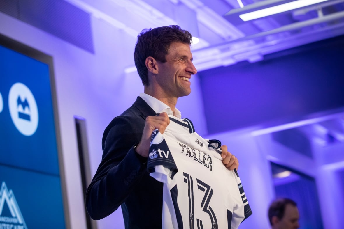 A man holds up a jersey that reads on the back Müller 13.