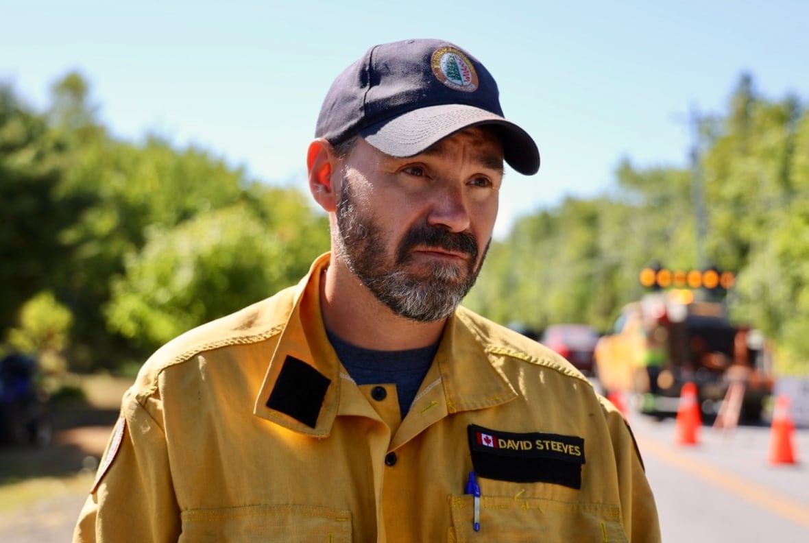 A man in a yellow uniformed shirt with a name badge speaks with a reporter.