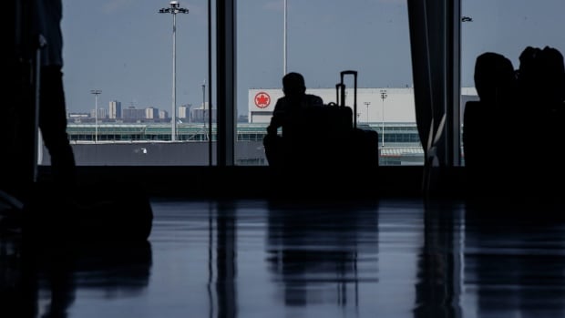 A person's silhouette is shown against a window, with the Air Canada logo visible on a building in the background.