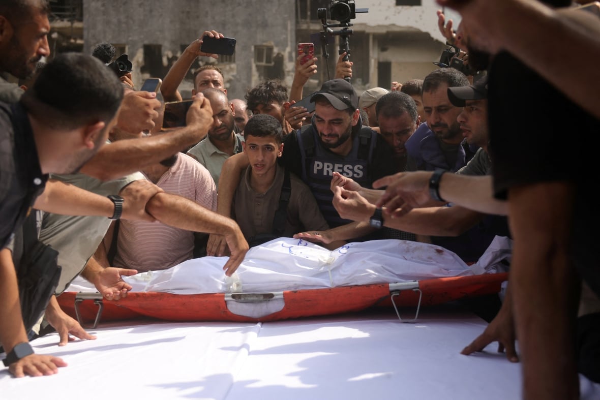 Mourners surround a shrouded body that is lying on a table outside.