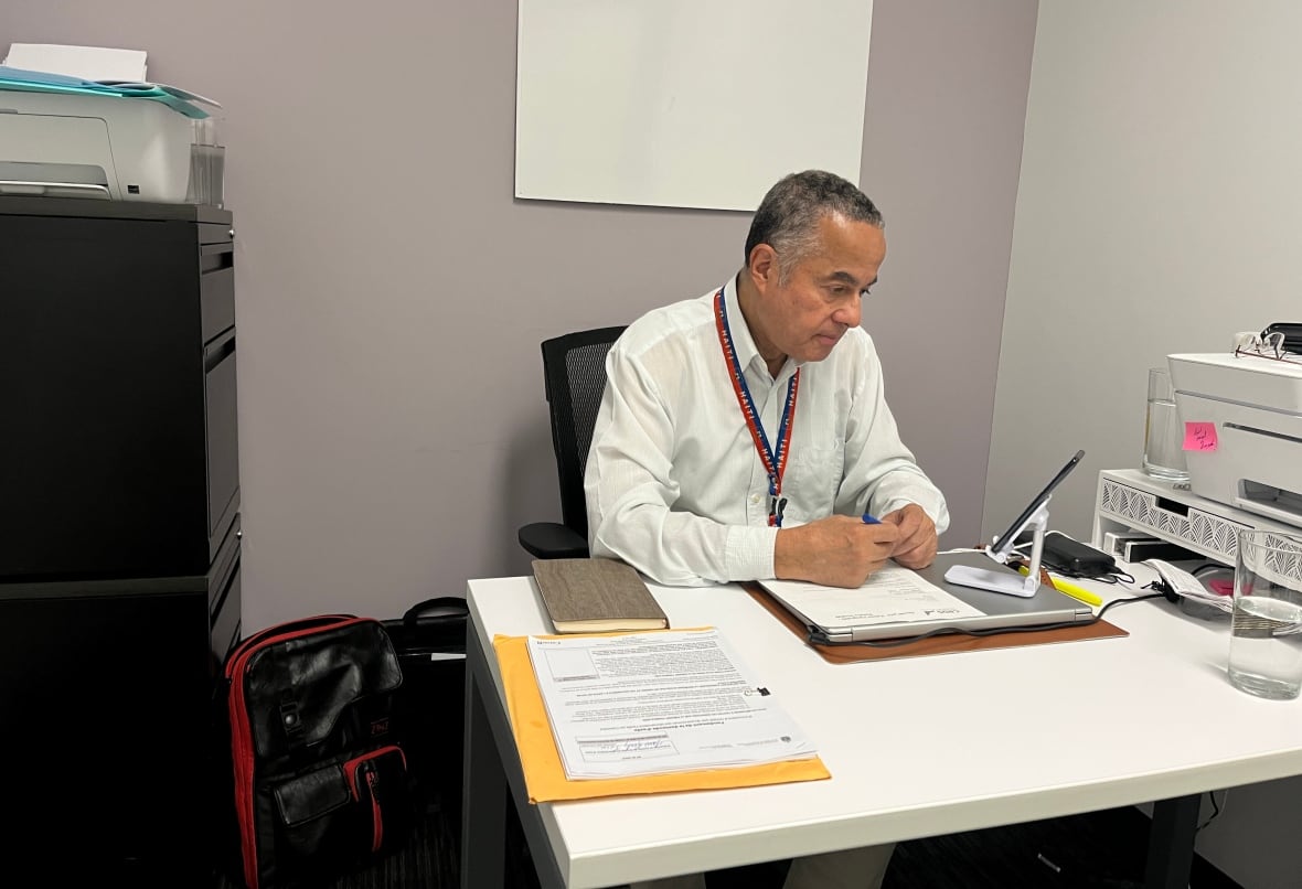 A man sits at a desk in a small office.