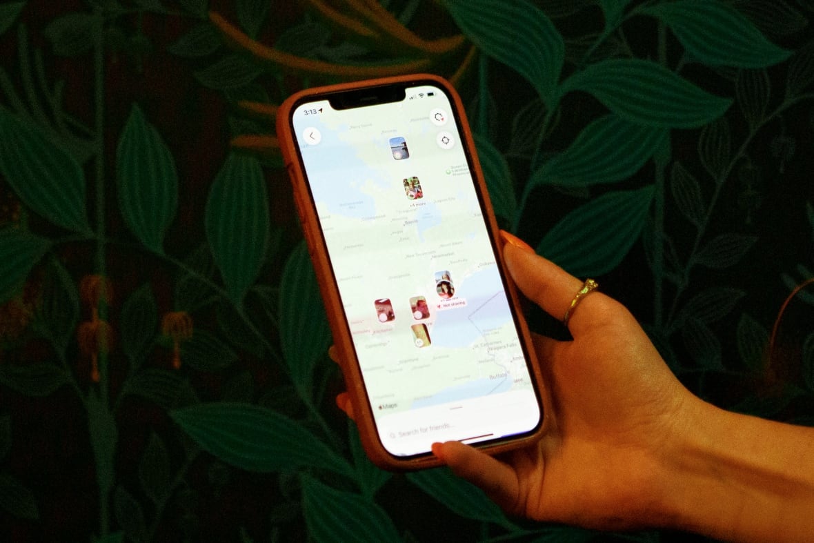 Una mano tiene un iPhone e sullo schermo è visibile una mappa che mostra le posizioni segnate dagli utenti.