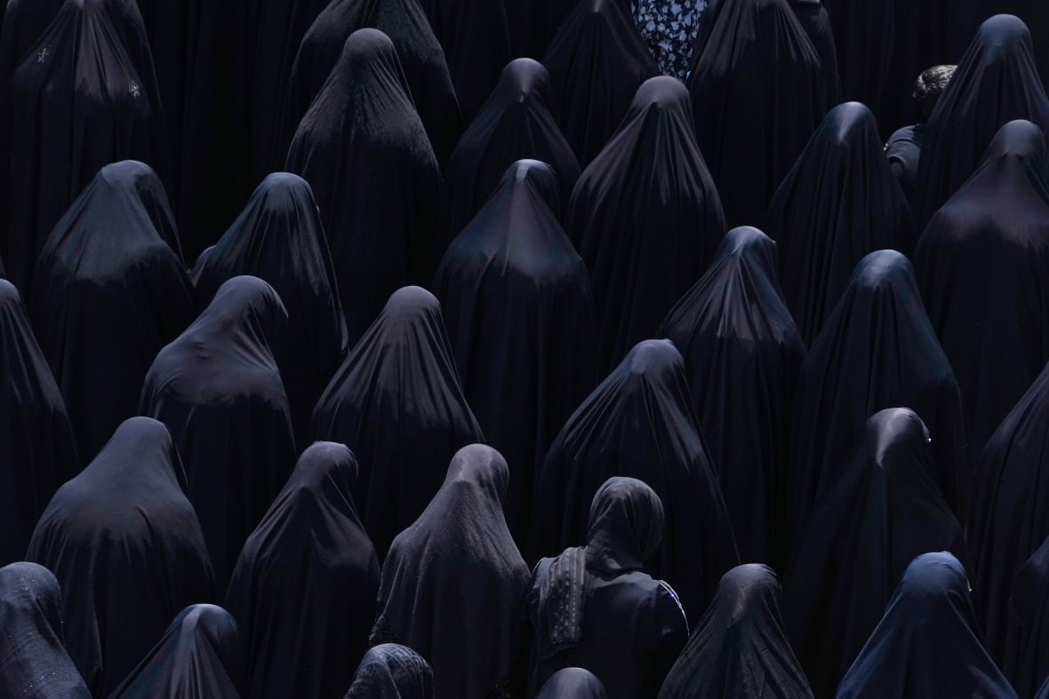 Rows of women covered in dark niqabs, praying.