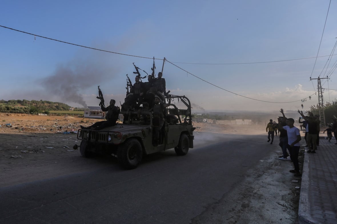 Smoke rises in the background as Hamas gunmen cruise the streets of Gaza in an Israeli military vehicle that was seized after they infiltrated areas of southern Israel, in the northern Gaza Strip, October 7, 2023.