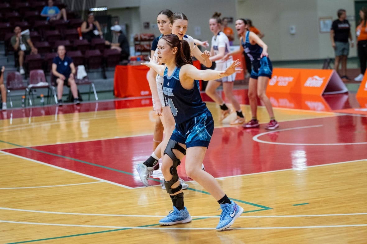 A basketball player in dark blue jersey wearing a knee brace with her arms outstretched during a basketball game.