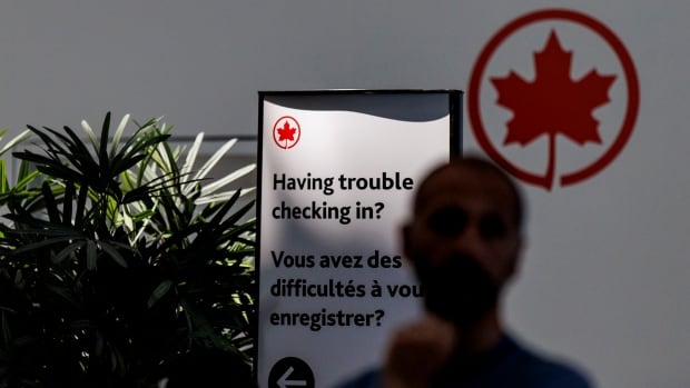 A person stands in front of a sign that reads, 'Having trouble checking in?'