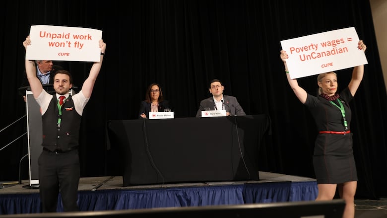 Flight attendants in uniform hold signs that read: Unpaid work won'd fly and Povery wages is UnCanadian, in front of two airline executives who are holding a news conference.