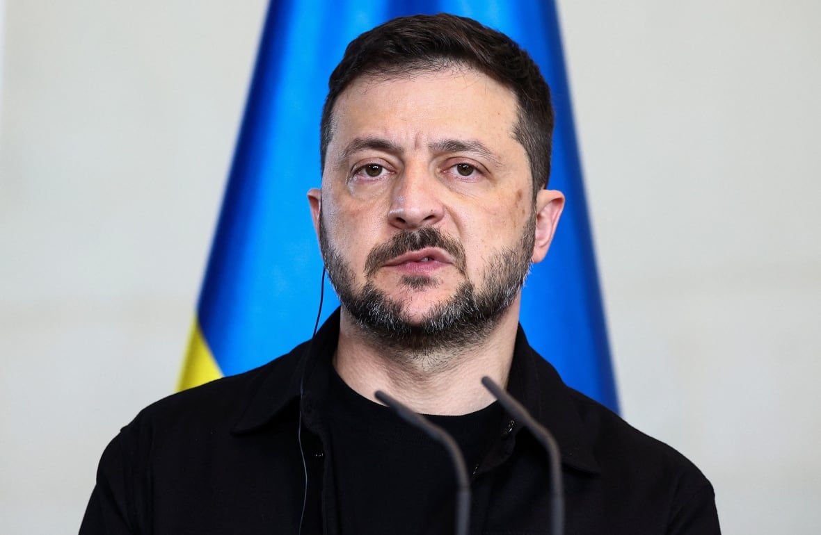 A man with a black beard and dressed in black stands in front of a microphone.