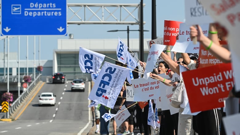 People holding signs demonstrate beside a road.