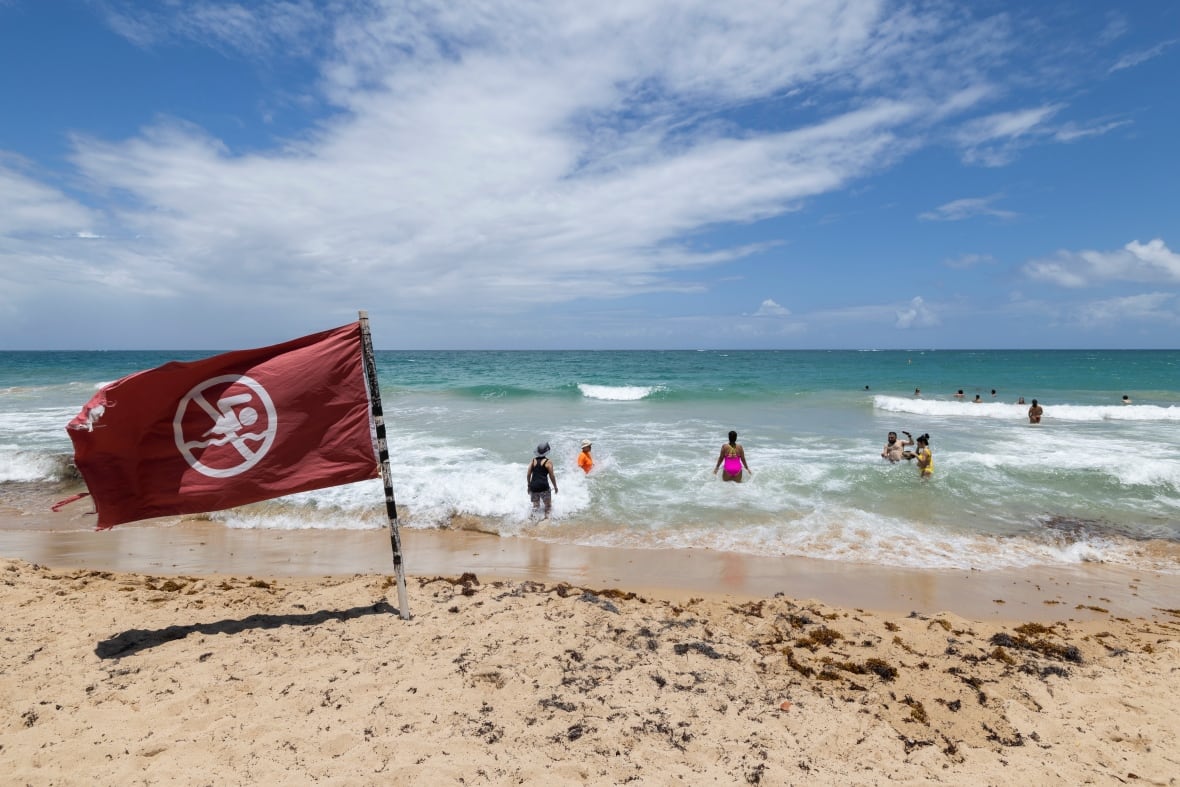A flag warning people not to swim is seen on a beach as people wade into the water.