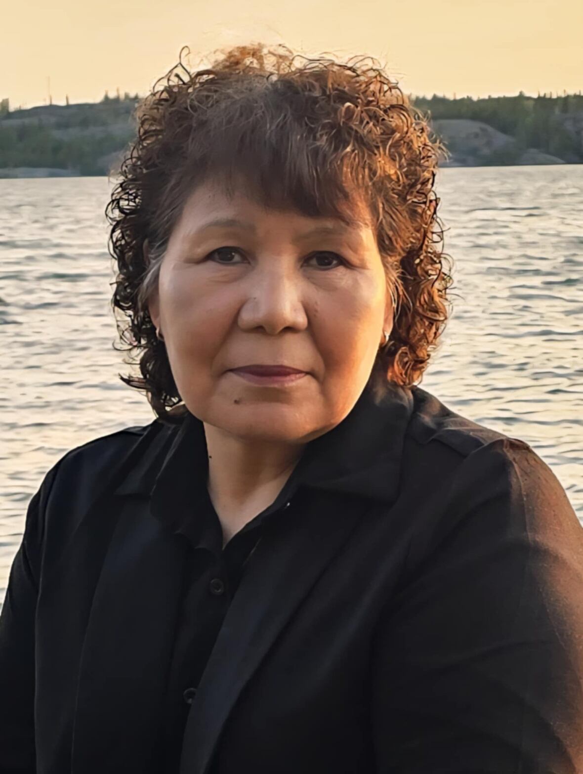 A woman sits in front of a body of water.