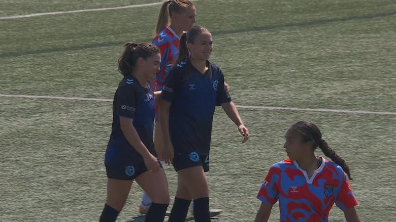 Two female soccer players smile on the field.