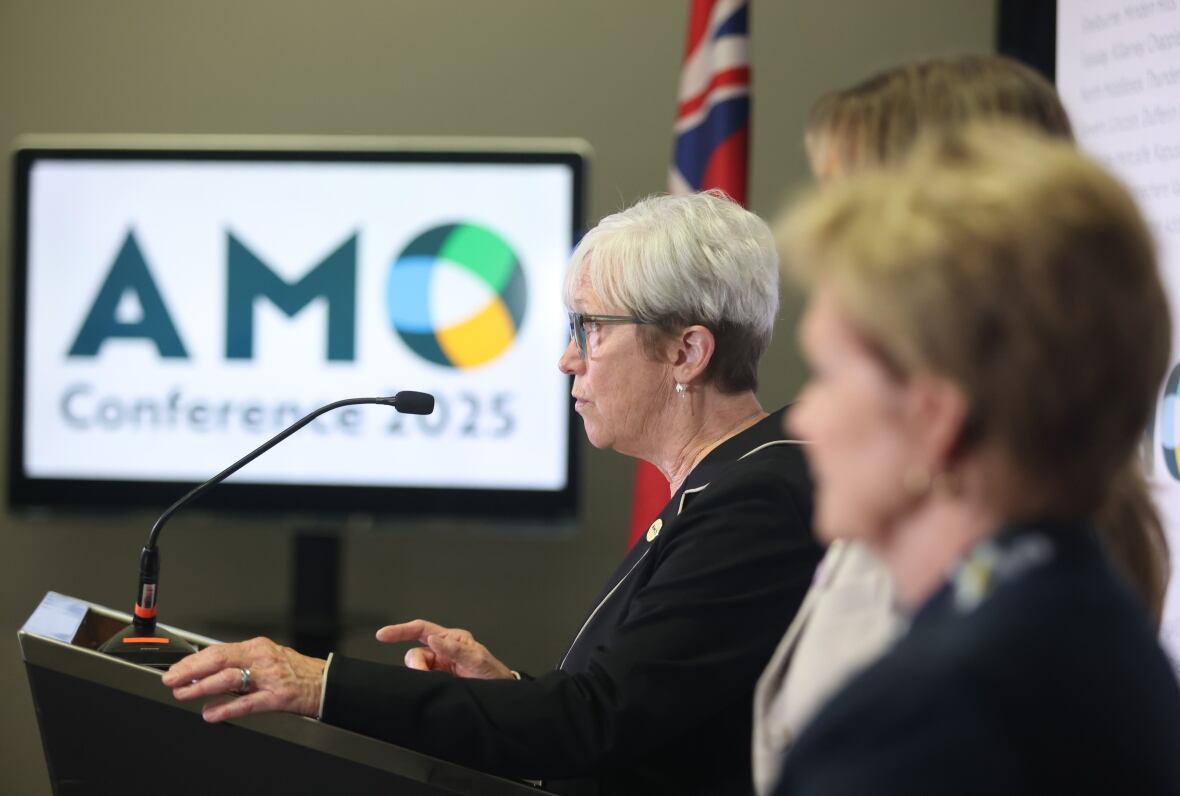 A woman speaks at a podium into a microphone while another woman stands next to her.